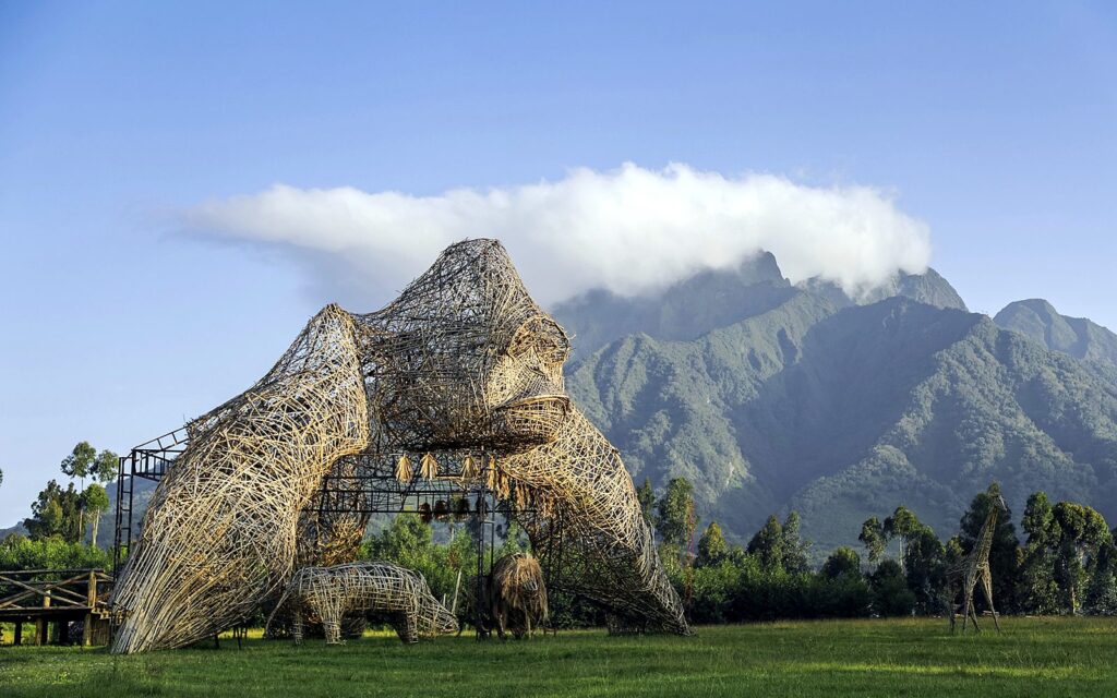 Giant woven bamboo gorilla sculpture on a lawn in front of green volcanic mountains