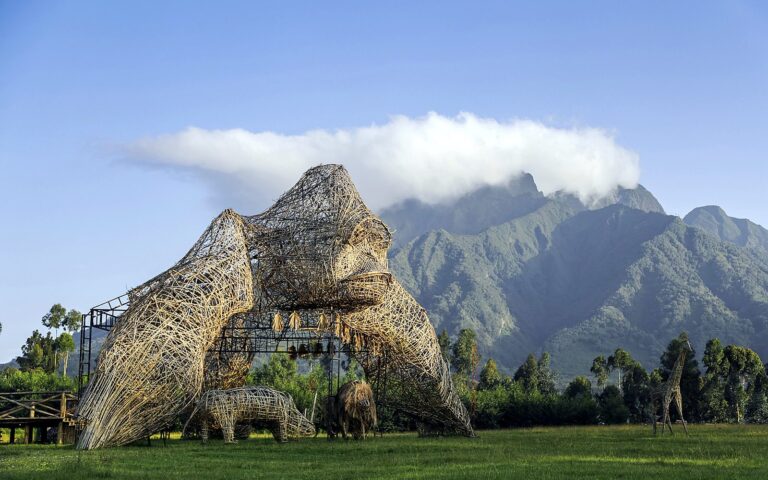 Giant woven bamboo gorilla sculpture on a lawn in front of green volcanic mountains